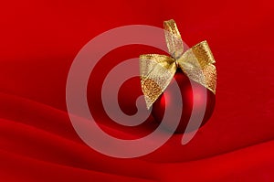 Elegant christmas background with traditional red christmas ball with gold shiny ribbon stand on scarlet smooth wavy silk.