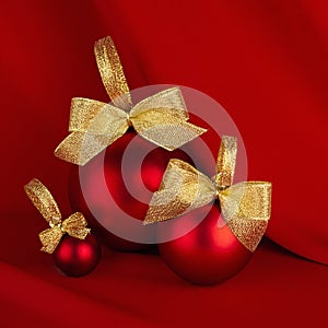 Elegant christmas background with traditional red christmas ball with gold shiny ribbon stand on scarlet smooth wavy silk, square.