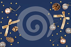 Elegant Christmas flat lay with golden and silver tree ornament baubles, ribbons and fir cones on sides of dark blue background