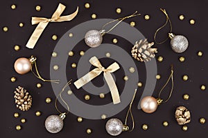 Elegant Christmas flat lay with golden tree ornament baubles, ribbons and fir cones on black background