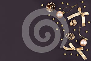 Elegant Christmas flat lay with golden tree ornament baubles, ribbons and fir cones on dark black background with copy space