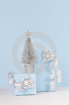 Elegant christmas gift boxes with shiny silver christmas tree on white wooden background and pastel blue wall.