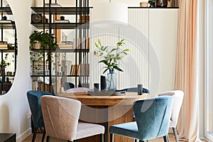 Elegant composition of stylish dining room interior design with velvet armchairs, design rounded wooden table and beautiful.