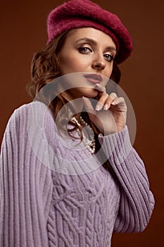 An elegant, confident, curly-haired young woman in a knitted beret and jacket.