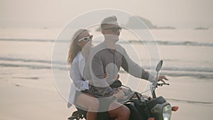 Elegant couple ride motorcycle along sea beach on sunrise. Intraframe installation from bike to people. Tourists drive