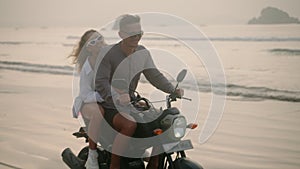 Elegant couple ride motorcycle along sea beach on sunrise. Intraframe installation from people to bike wheels. Tourists