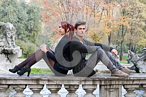 Elegant couple sitting back to back on stone balusters