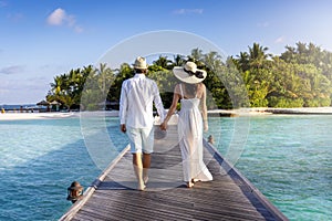 A elegant couple walks down a wooden pier over turquoise sea in the Maldives