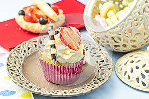 Elegant, creamy cupcake decorated with fruits, chocolate, and gold sprinkles on a romantic plate. Patisserie dessert with coffee i