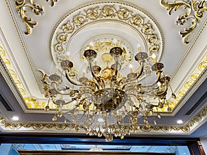 Elegant crystal chandelier hanging on the gilded gold ceiling. Luxury living room ceiling decoration
