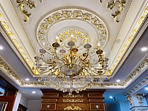 Elegant crystal chandelier hanging on the gilded gold ceiling. Luxury living room ceiling decoration