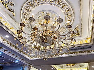 Elegant crystal chandelier hanging on the gilded gold ceiling. Luxury living room ceiling decoration