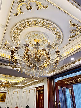 Elegant crystal chandelier hanging on the gilded gold ceiling. Luxury living room ceiling decoration