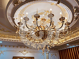 Elegant crystal chandelier hanging on the gilded gold ceiling. Luxury living room ceiling decoration