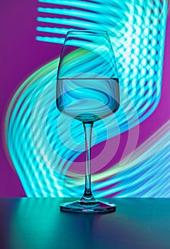 Elegant crystal glass filled with pure water on a purple background painted with blue light. Light reflections and refractions,