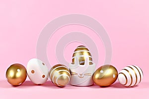 Elegant golden and white painted easter eggs with dots and stripes and cute easter egg cup in shape of bunny on pink background