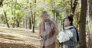 Elegant elderly, lovely couple with bouquet of flowers walks in park, has a talk