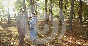 Elegant, elderly woman talking with man with crutch in autumn park