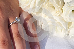 An elegant engagement diamond ring on a woman`s hand and a bouquet of white Lisianthus flowers