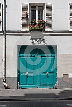 Aquamarine color gates of old building with red flowers on window with opened white shutters. Classical style door.