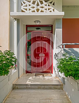 An elegant family house entrance with dark red door and plants.
