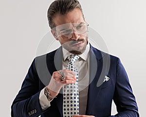 elegant fashion man with glasses looking away while fixing high class tie