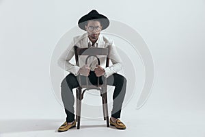 elegant fashion man with hat and glasses holding chair's back