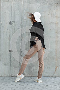 Elegant fashion model young woman in stylish glasses in black blazer in beige pants in casual shoes and fashionable straw hat near