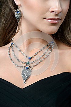 Elegant fashionable woman with jewelry. Beauty young model with a silver pendant on a dark background