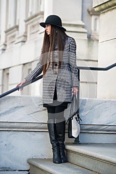 Elegant and fashionable young businesswoman standing oudoors holding a bag wearing hat