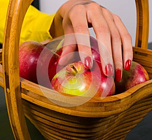 Elegant female hand picking apple from wooden basket