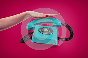 An elegant female hand presses down a handle of a retro blue rotary phone that rings and almost jumps up.
