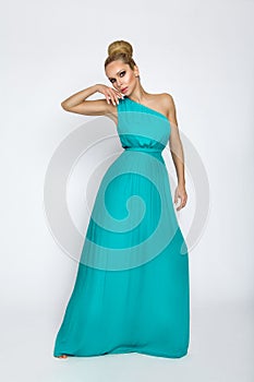 Elegant female model in a turquoise long silk dress standing on a white background