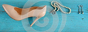 Elegant female shoes, pearl necklace and earrings on a blue background. Wide photo