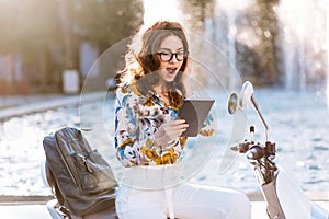 Elegant female student with leather backpack and map-case reading something with surprised face. Emotional brunette girl