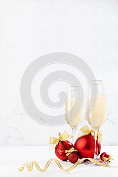 Elegant festive Christmas background with fizz champagne in glasses with shiny red balls and golden ribbon as decor on soft light.