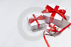 Elegant festive classic white gift boxes with red bow, ribbon on white wood board, copy space, background for shopping.