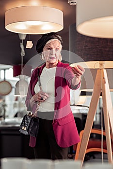 Elegant French-style aging cheerful dame standing in lighting showroom