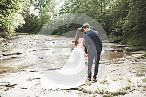 Elegant gentle stylish groom and bride near river with stones. Wedding couple in love