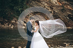 Elegant gentle stylish groom and bride near river with stones. Wedding couple in love