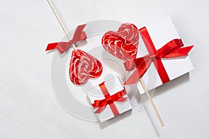 Elegant gentle wedding background - white gift boxes with red bow, sweet lollipops hearts on white wood board, top view.