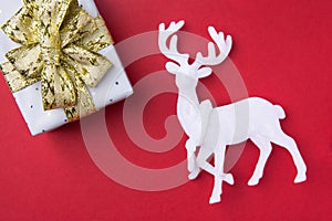 Elegant gift box wrapped in silver paper tied with golden ribbon bow white deer on dark red burgundy background. New Year