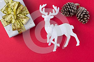 Elegant gift box wrapped in silver paper tied with golden ribbon bow white deer pine cones on dark red background. New Year