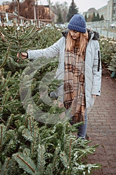 Elegant girl buys a Christmas tree. Womanin a blue cap and scarf. Beautiful lady with blond hair.