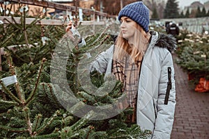 Elegant girl buys a Christmas tree. Womanin a blue cap and scarf. Beautiful lady with blond hair.