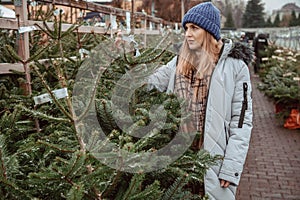 Elegant girl buys a Christmas tree. Womanin a blue cap and scarf. Beautiful lady with blond hair.