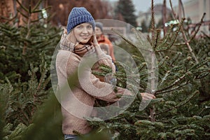 Elegant girl buys a Christmas tree. Womanin a blue cap and scarf. Beautiful lady with blond hair.