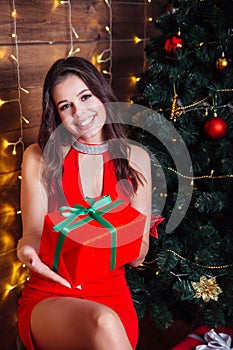 Elegant girl in red dress with gift box near christmas tree