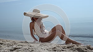 Elegant girl touching sand sitting beach in swimsuit. Happy woman sunbathing.