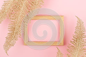 Elegant glamour background - gold decorative feathers and blank frame on soft light pastel pink background, top view, copy space.